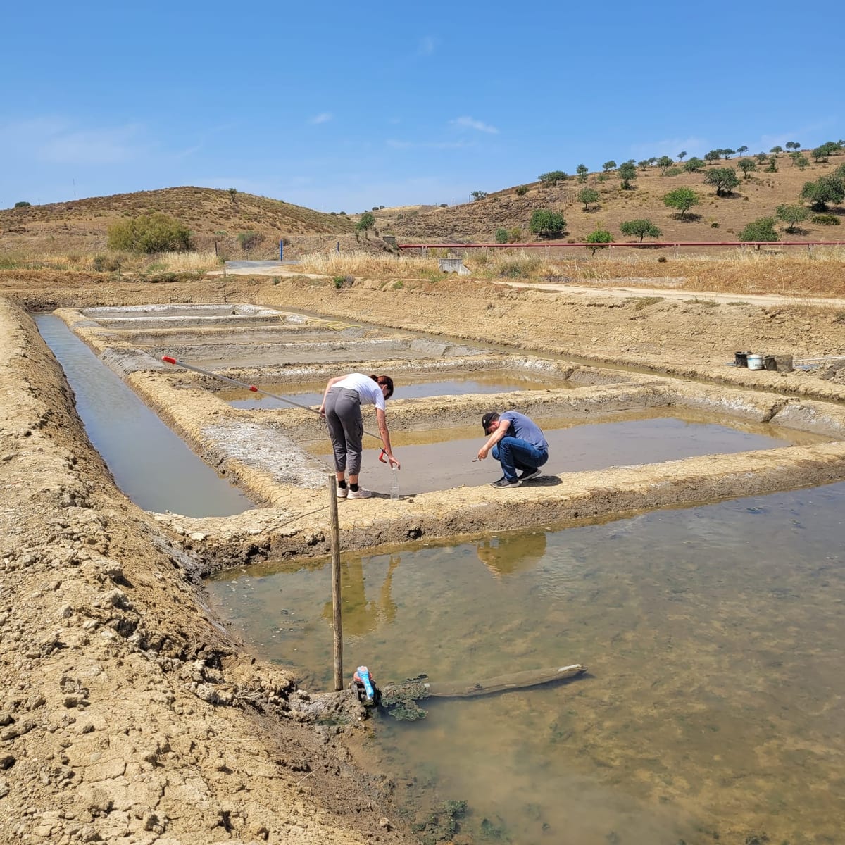 Two researchers sampling at the edge of the crystallisation pans.